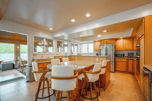 A modern kitchen with a large island, wooden cabinets, and a view of the outdoors.
