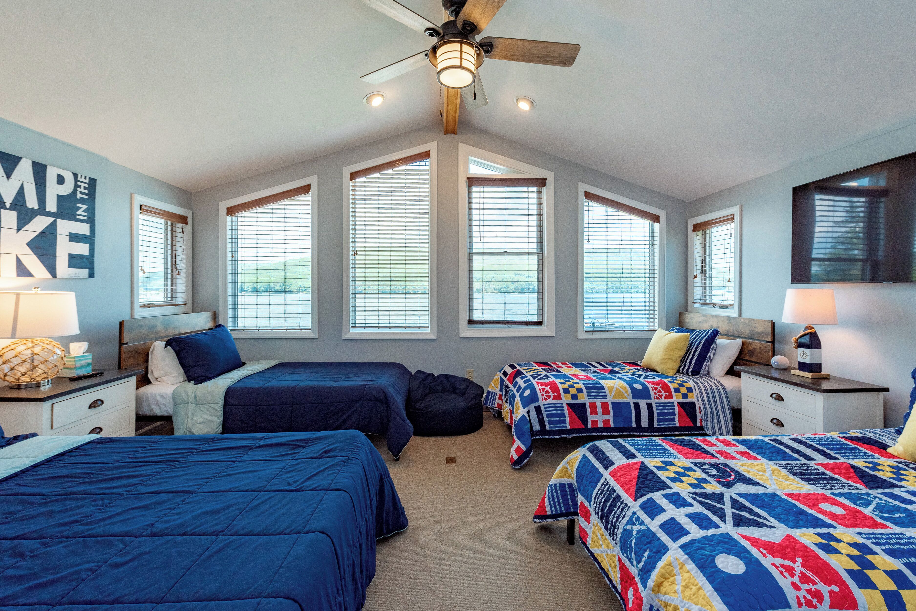 A bedroom with three beds, a ceiling fan, and large windows.