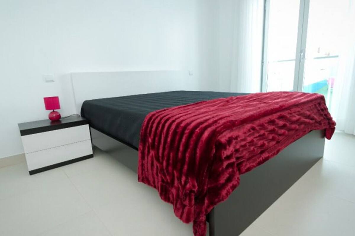 A bedroom with a bed, a nightstand, a lamp, and a window with curtains.