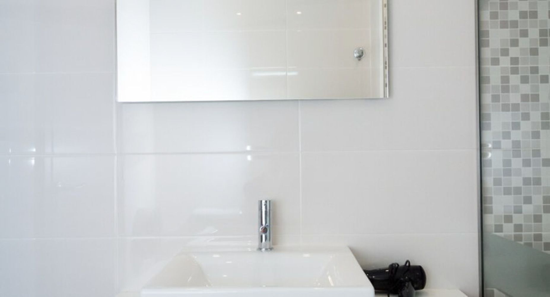 Un baño con un lavamanos blanco, un espejo y una zona de ducha con azulejos.