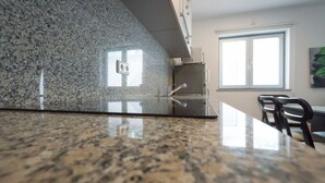 Una cucina con piani di lavoro in granito, lavello in acciaio inossidabile e una finestra con persiane.