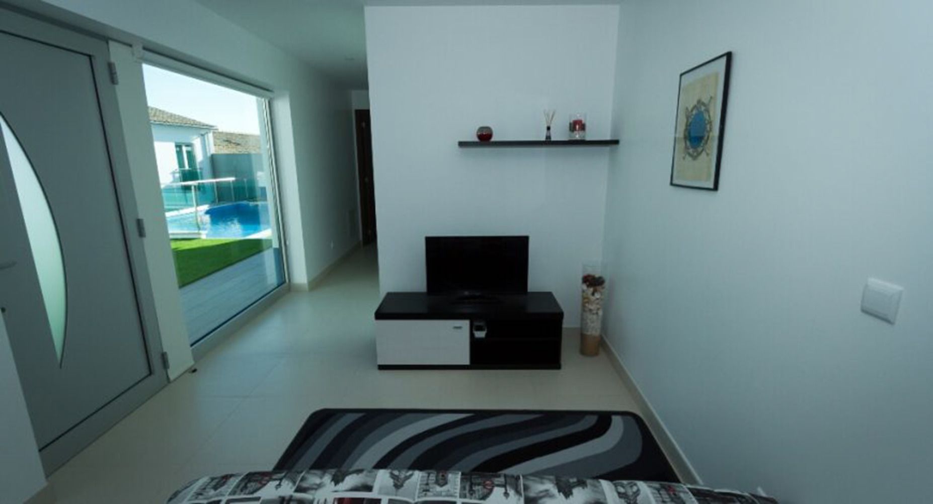 A modern living room with a flat-screen TV, a small cabinet, and a decorative shelf with items.