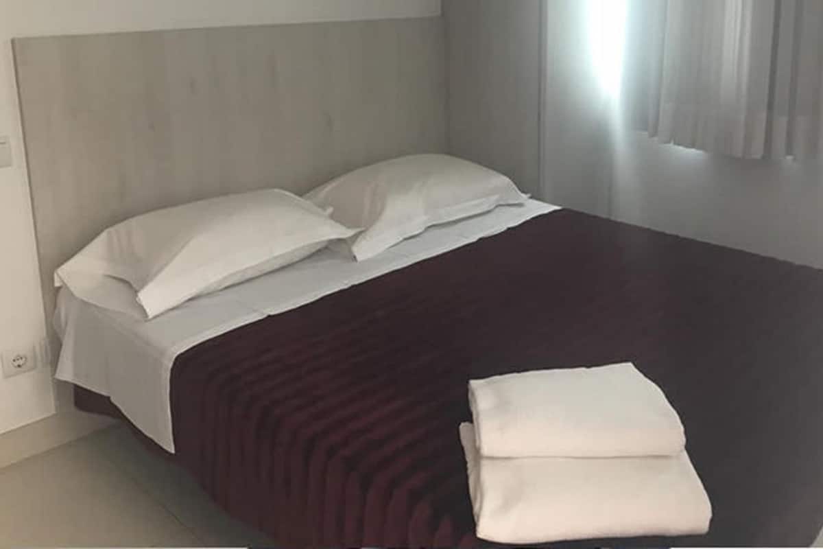A bedroom with a bed, pillows, a folded blanket, and a window with curtains.