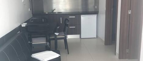 A modern apartment with a black sofa, a dining table, and a kitchen area.