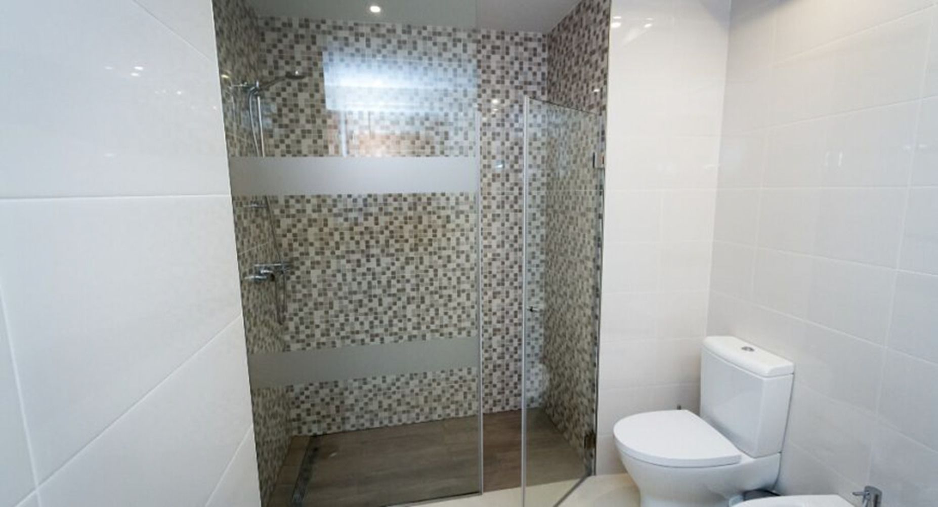 A bathroom with a shower, toilet, and tiled walls.