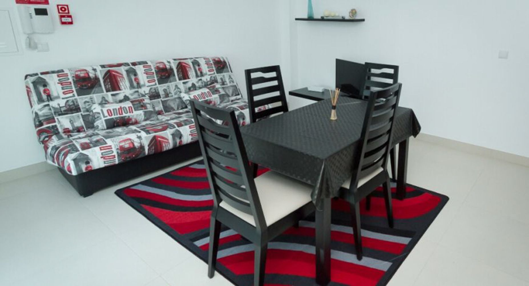 Uma área de refeições com uma mesa e cadeiras, um sofá com estampa temática de Londres e um tapete listrado em vermelho e preto.
