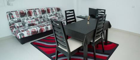 Uma área de refeições com uma mesa e cadeiras, um sofá com estampa temática de Londres e um tapete listrado em vermelho e preto.