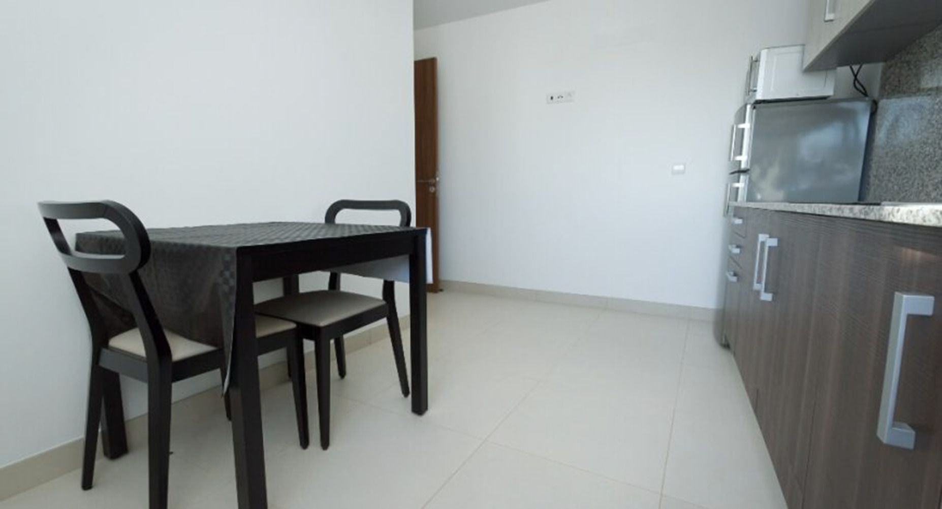 A small, modern kitchen with a dark countertop and cabinets, a table with chairs, and a door in the background.