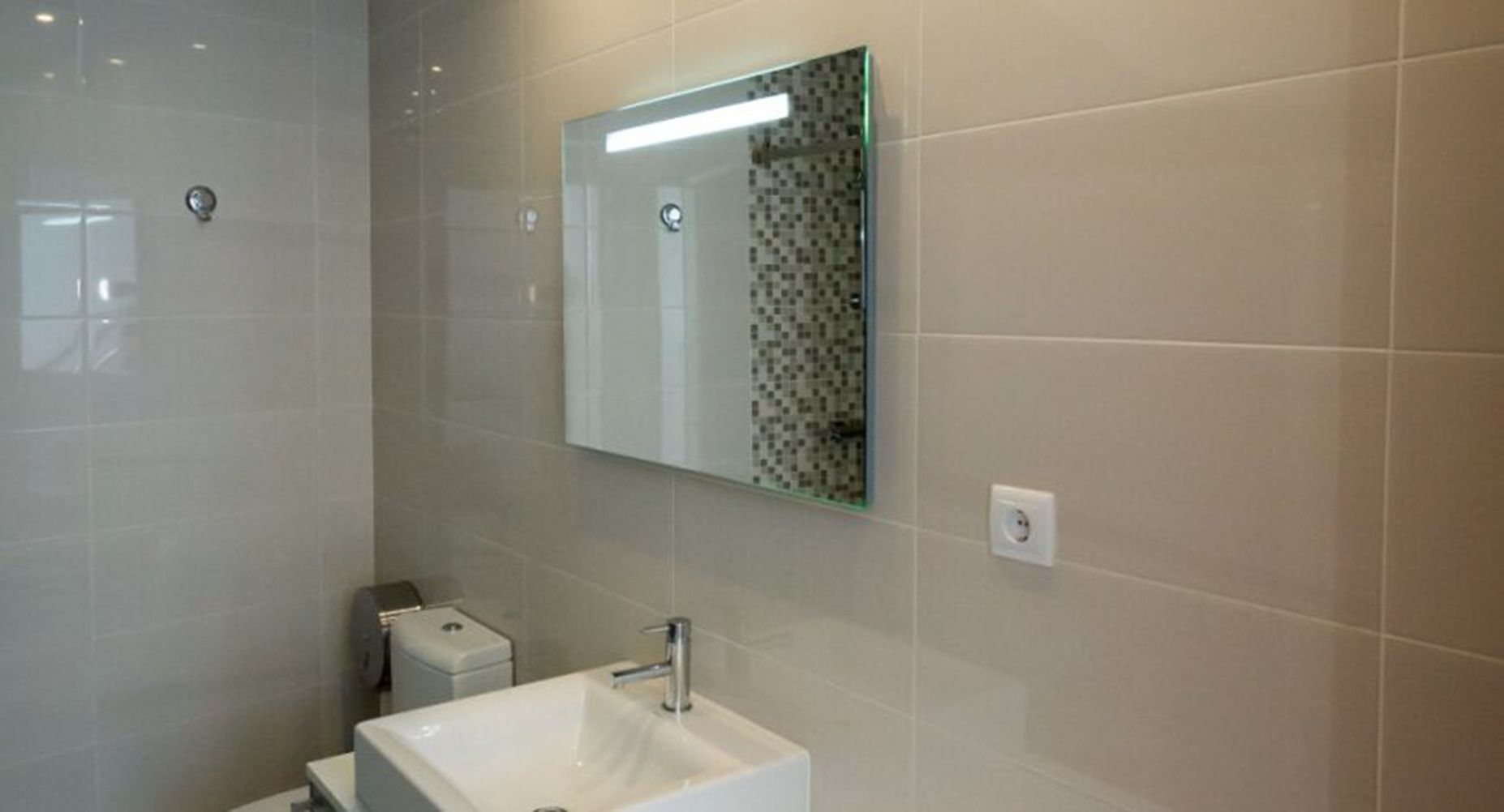 Ein modernes Badezimmer mit einem weißen Waschbecken, einem Spiegel und einer Duschkabine aus Glas.
