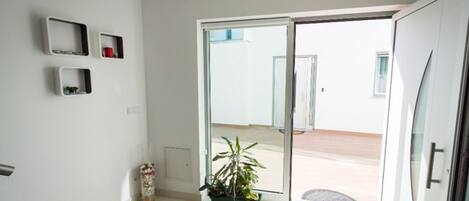 Een moderne kamer met een schuifdeur naar een buitenruimte. Tegen de wand staan drie witte planken, een potplant en een klein decoratief object op de vloer.