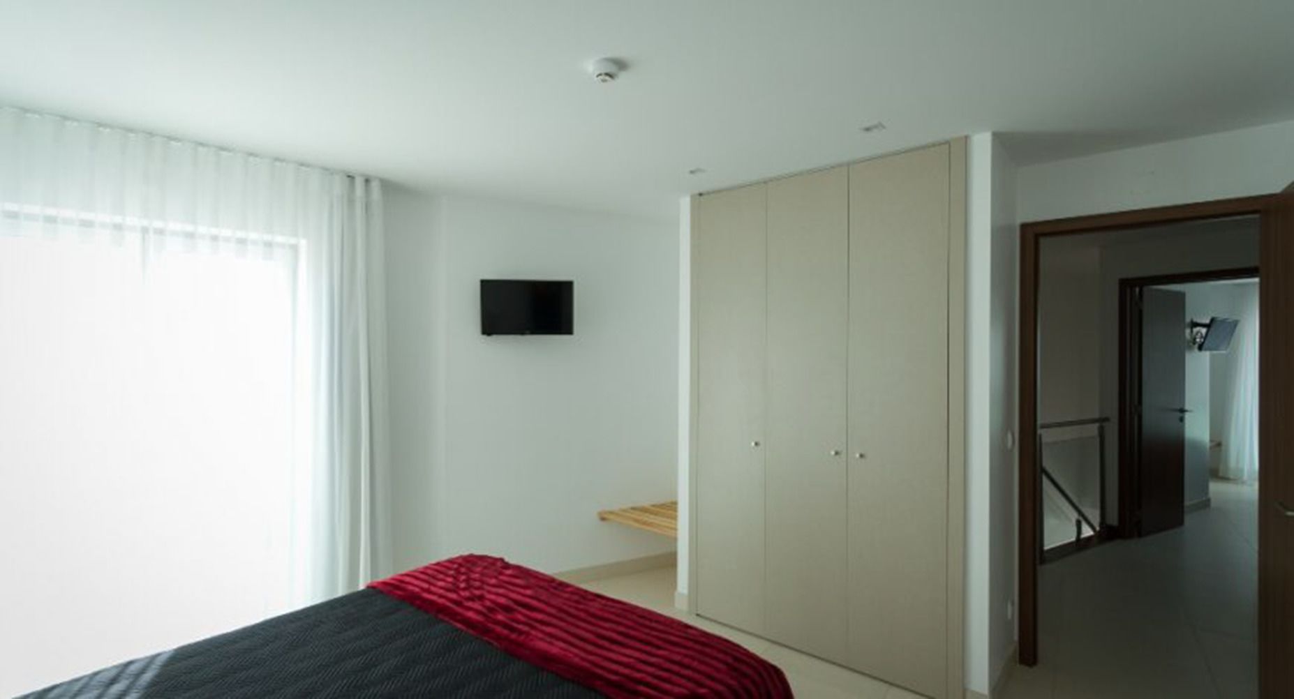 A bedroom with a bed, a wardrobe, a television, and a door leading to another room.