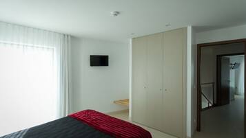 A bedroom with a bed, a wardrobe, a television, and a door leading to another room.