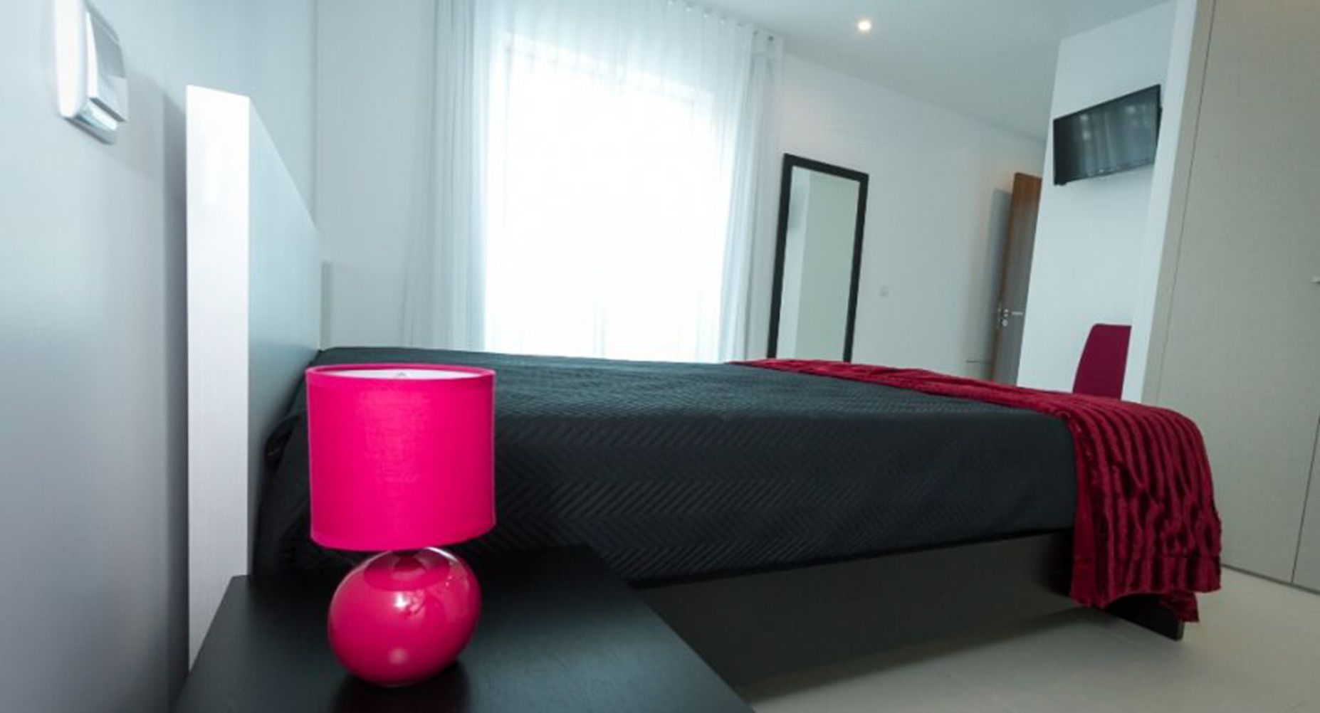 A modern hotel room with a bed, a bedside table with a lamp, and a TV mounted on the wall.