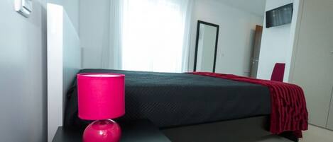 A modern hotel room with a bed, a bedside table with a lamp, and a TV mounted on the wall.