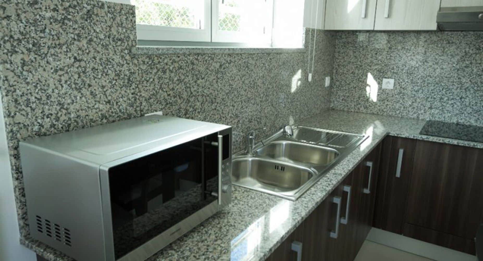 Una cocina con encimeras de granito, pileta de acero inoxidable y alacenas de madera.