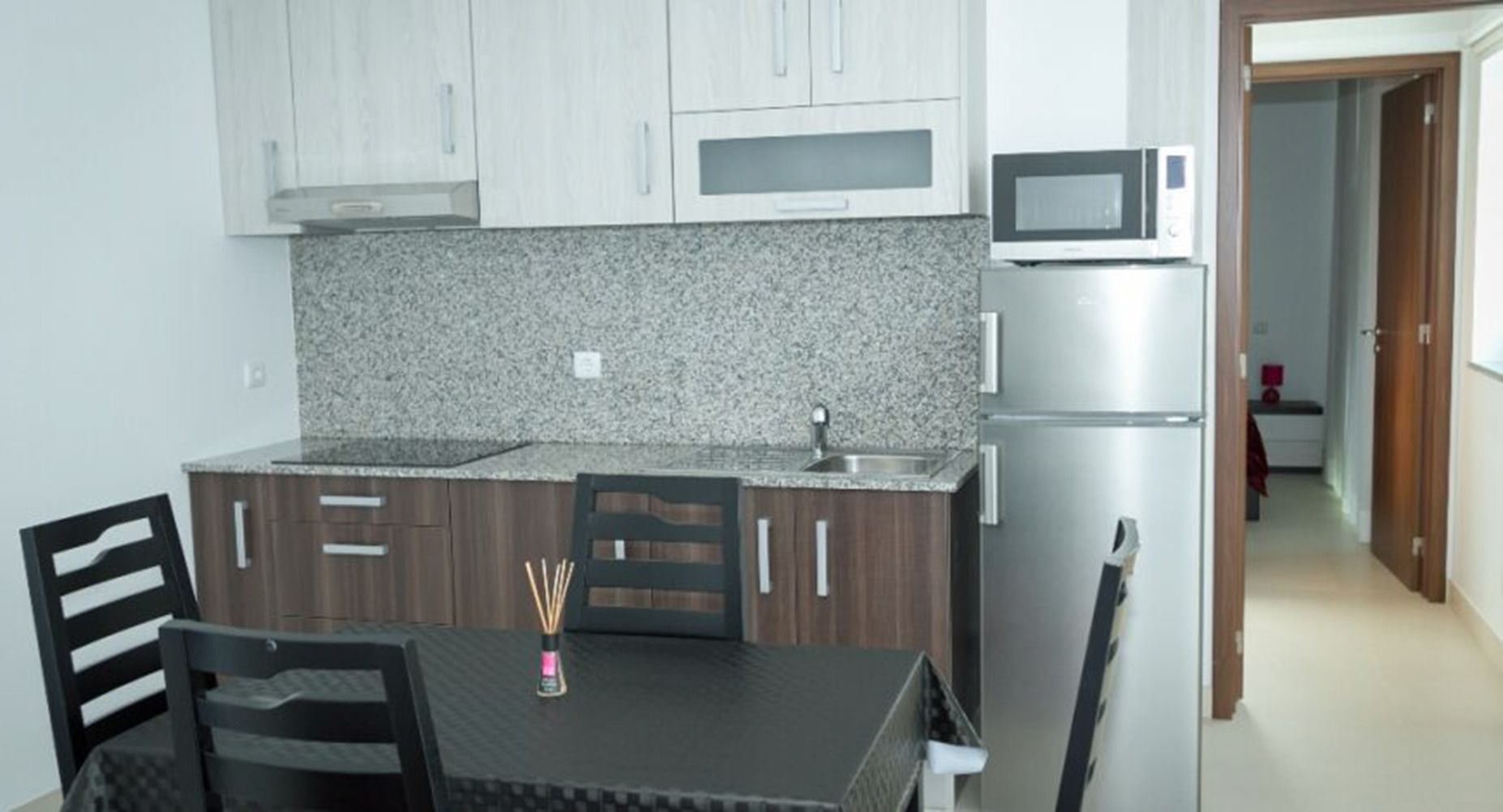 A compact kitchen with granite countertops, a microwave, a refrigerator, and a dining table with chairs.