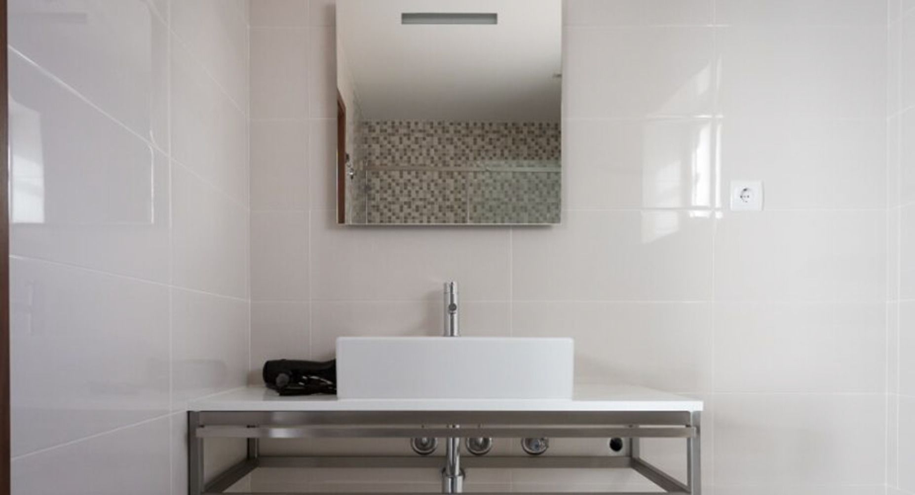 Un baño moderno con un lavamanos blanco, un espejo encima y un salpicadero de azulejos con diseño.