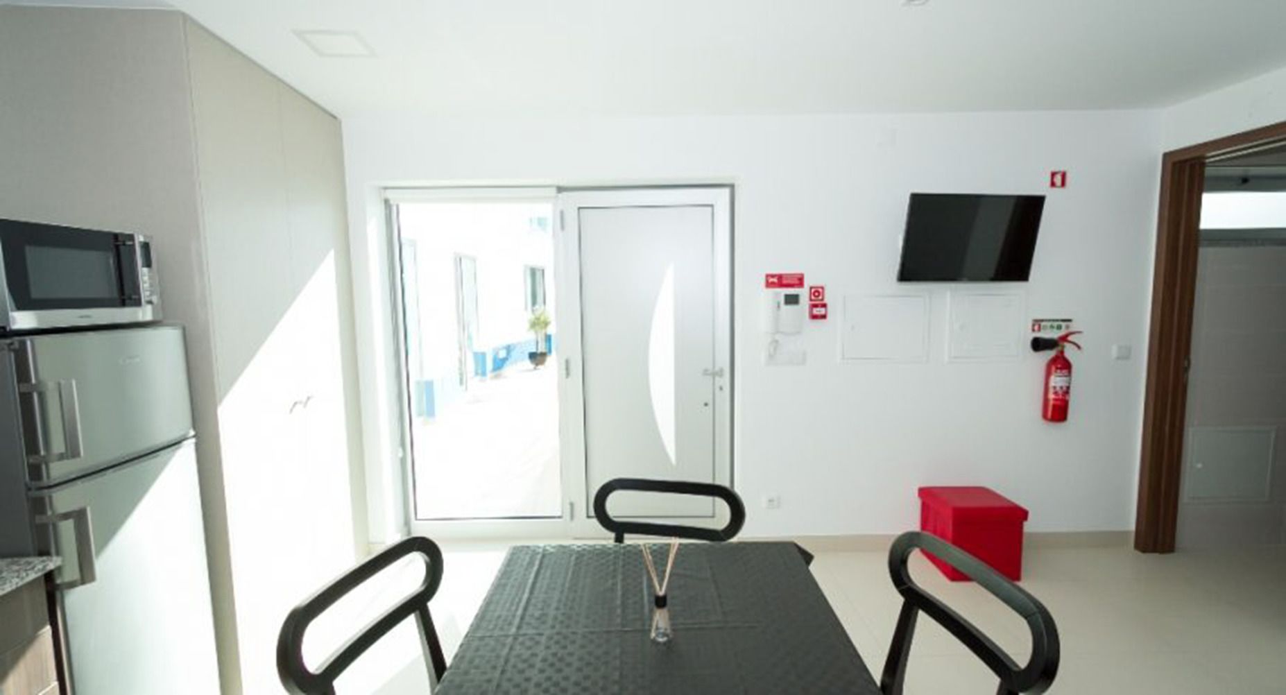 Una cocina moderna con electrodomésticos de acero inoxidable, una mesa de comedor con sillas, un extintor de incendios y un televisor montado en la pared.