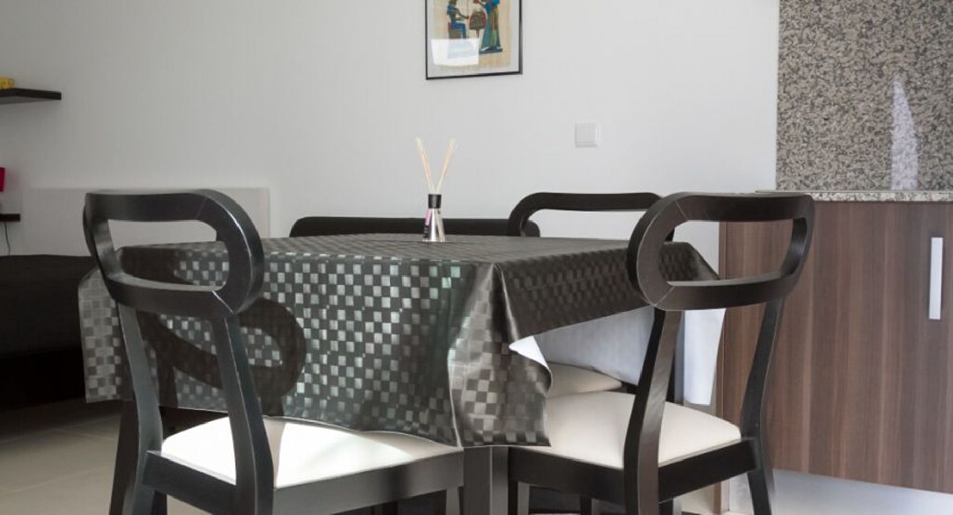 A dining area with a table covered in a checkered tablecloth, surrounded by four chairs with cushioned seats.