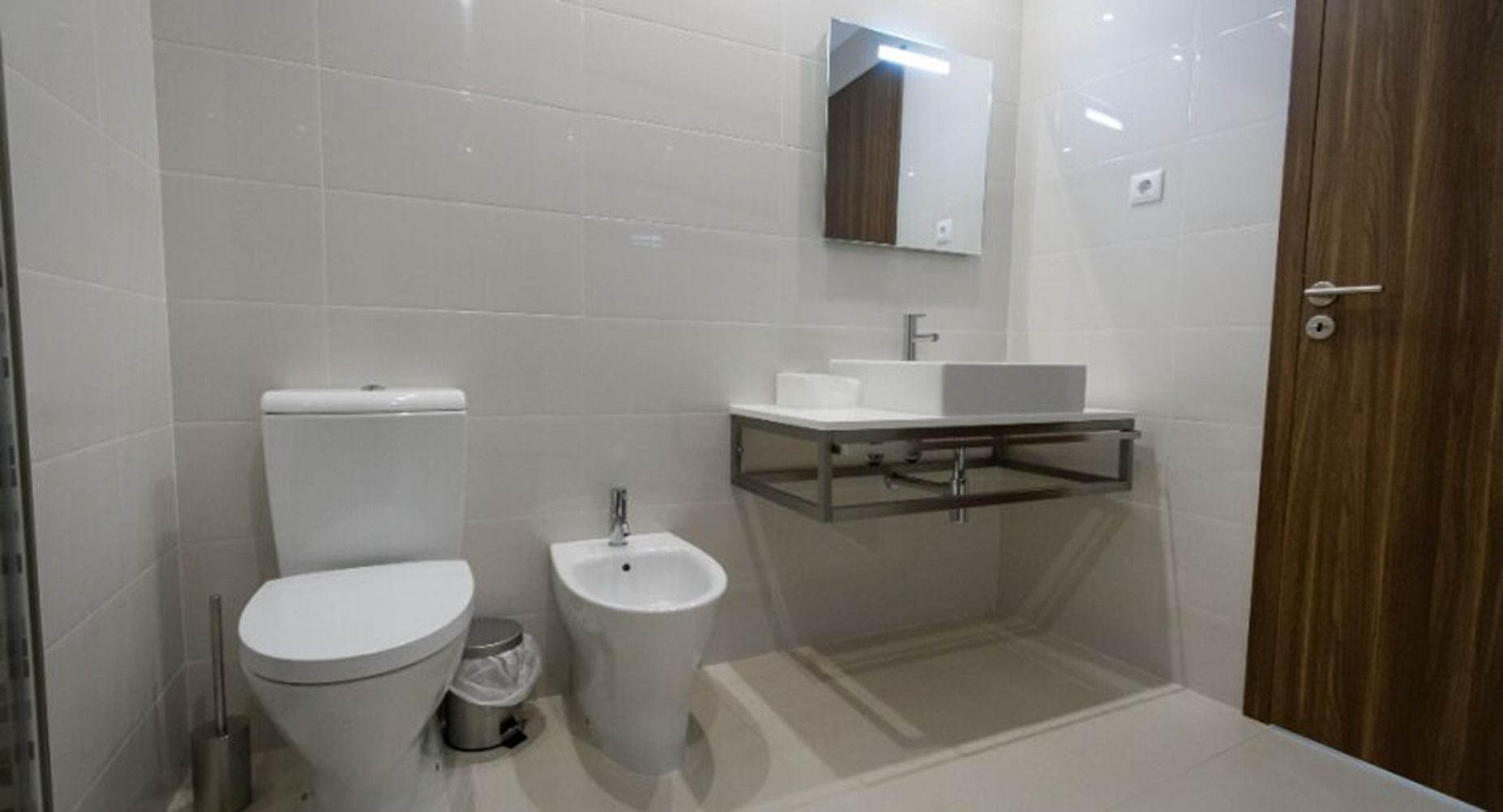 Un bagno moderno con toilette, bidet e lavandino con specchio sopra.