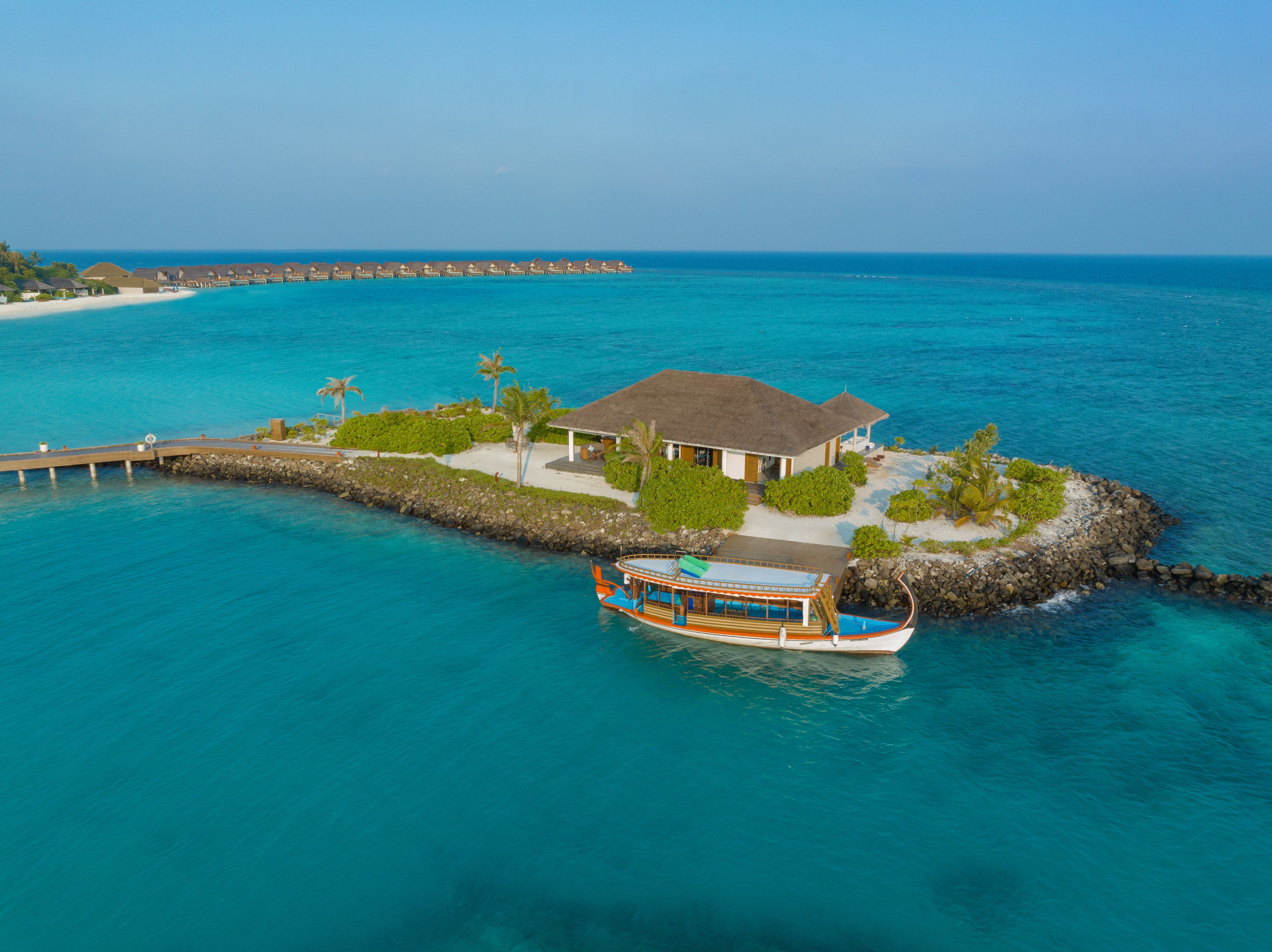 A tropical island with a bungalow, a pier, and a boat.