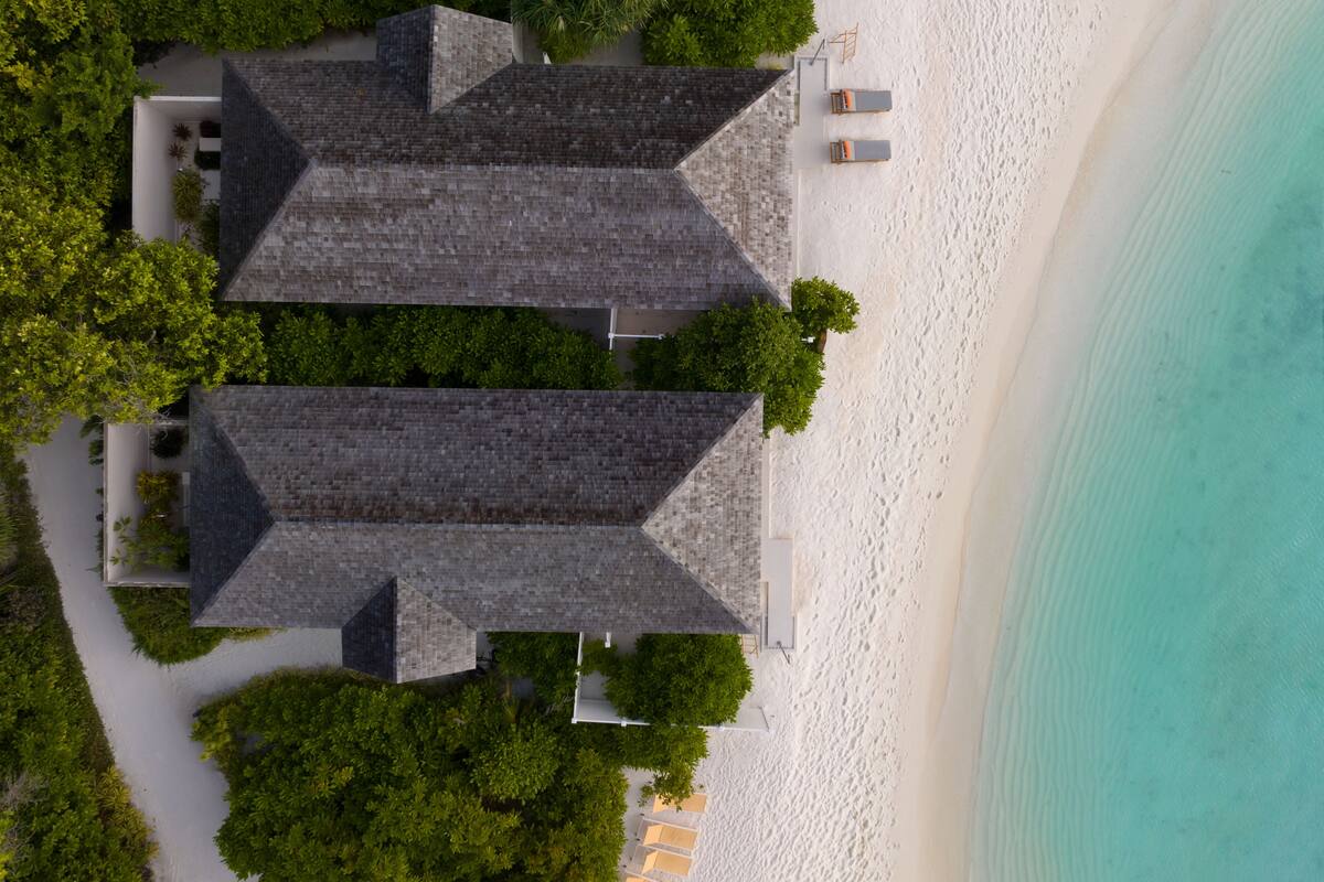 Ein Küstenanwesen mit zwei markanten Gebäuden, einem Sandstrand und einem klaren türkisblauen Meer.