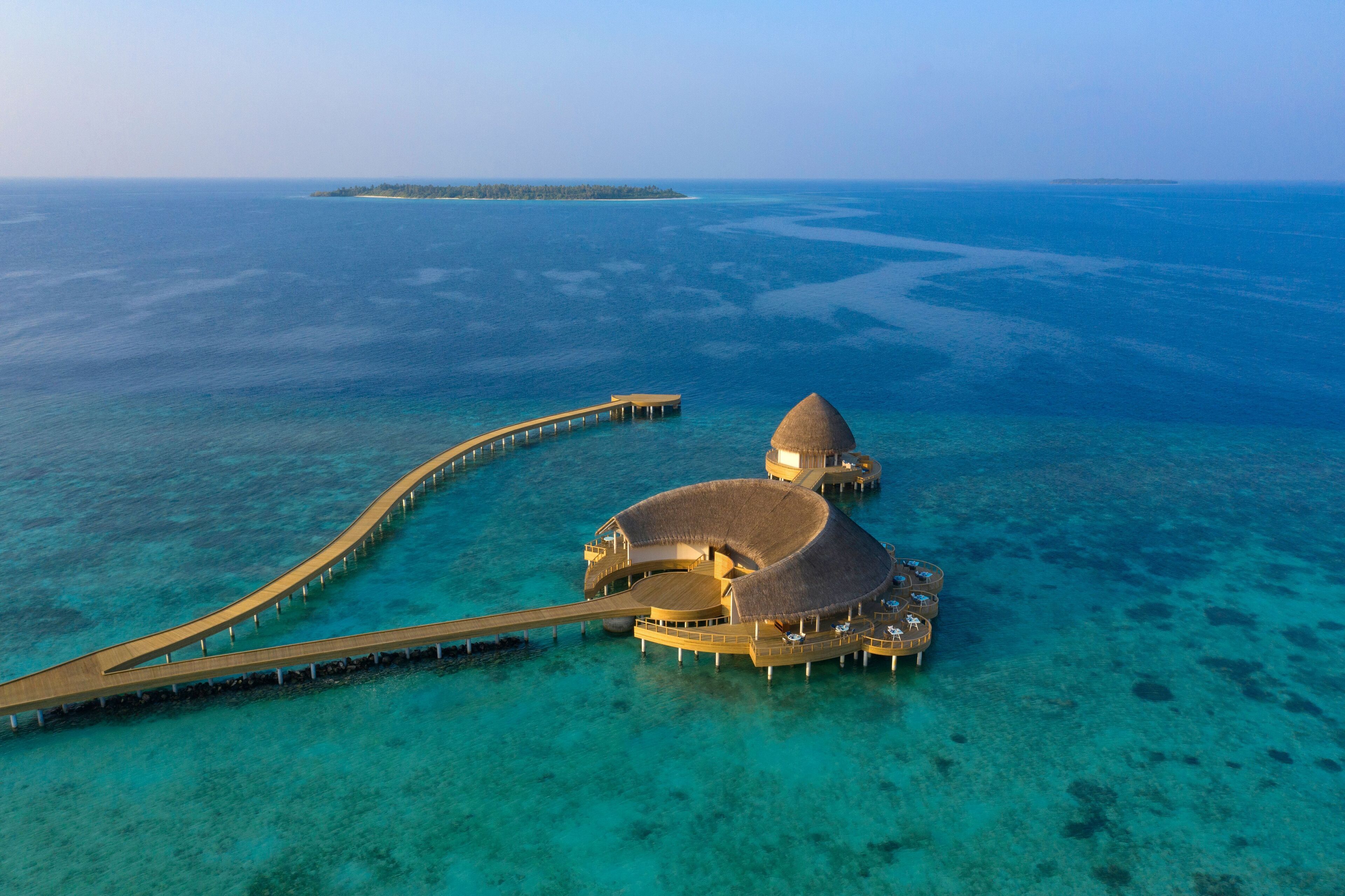 Een overwaterresort met een koepelvormig gebouw, een lange steiger en helder turquoise water.