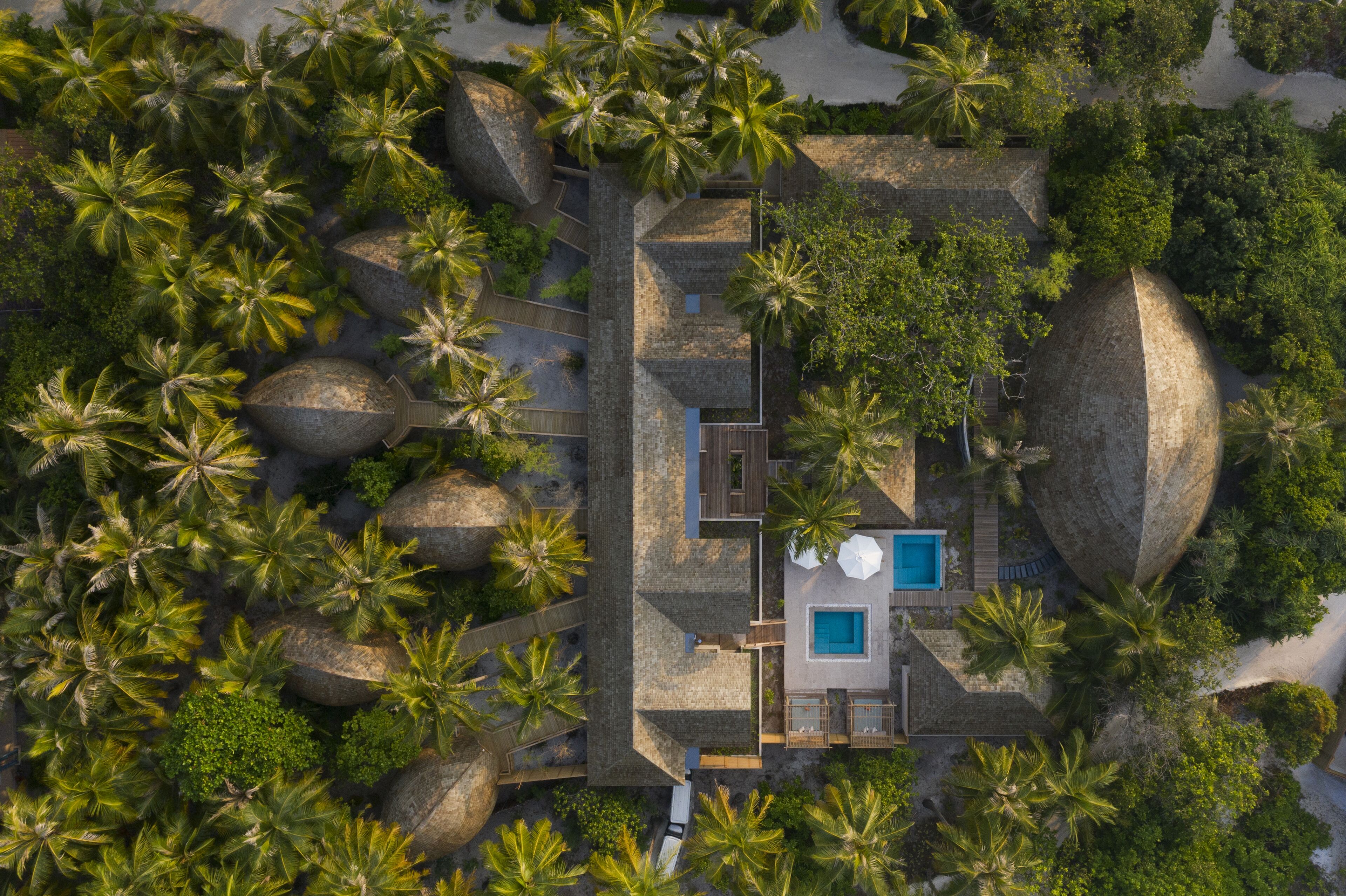 An aerial view of a resort with a swimming pool, palm trees, and stone structures.