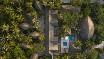 An aerial view of a resort with a swimming pool, palm trees, and stone structures.
