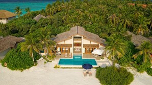 Une propriété située en bord de mer, dotée d’une piscine, de constructions à toits de chaume et d’une végétation luxuriante de palmiers.