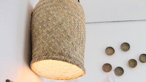 A wooden table with a framed menu, a woven light fixture, and white pillows on a bed. - Hotel Mamá Carlota (Querétaro)