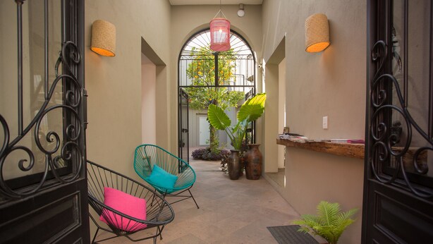 An indoor corridor with a wrought iron gate, a potted plant, and a chair with a cushion. - Hotel Mamá Carlota (Querétaro)