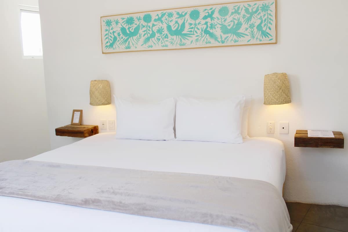 A neatly made bed with white linens, two wall-mounted lamps, and a framed artwork above the bed.