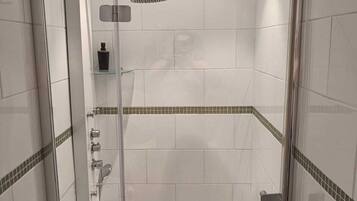 A modern shower area with a glass door, a handheld showerhead, and a built-in shelf.