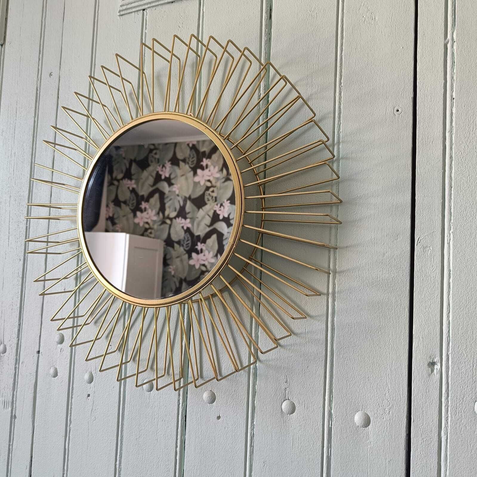 A round mirror with a gold frame mounted on a white wooden wall.
