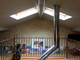 Una habitación con techos altos, pared de piedra, escalera metálica y tragaluz.