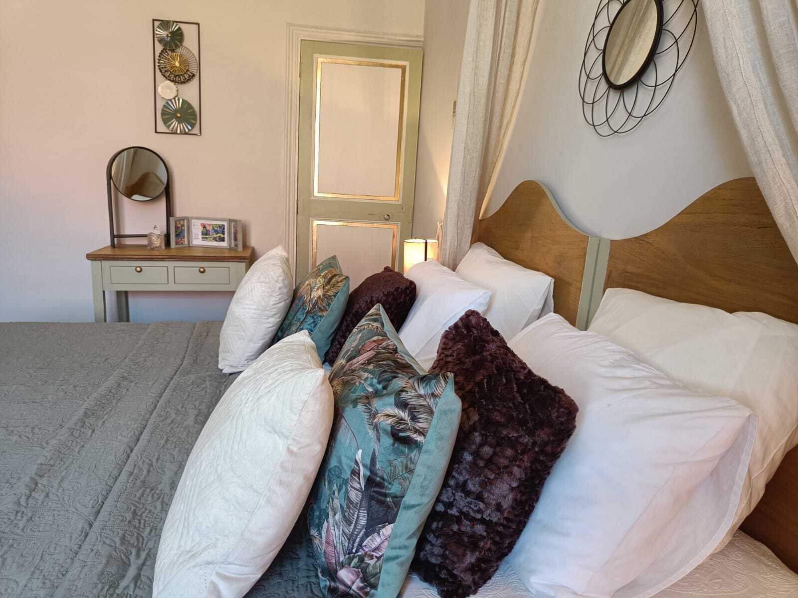 A neatly made bed with a variety of pillows, a bedside table with a lamp, and wall art.