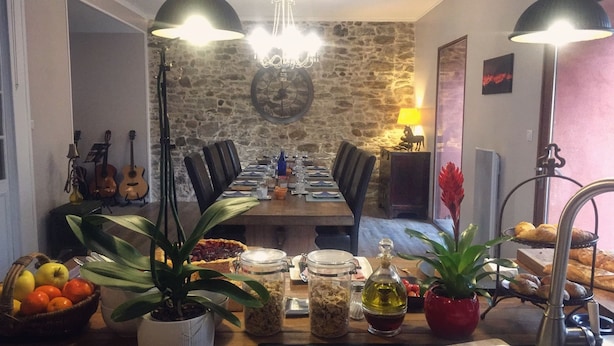 Een eetgedeelte met een stenen muur, een kroonluchter en een tafel voor vier compleet met diverse gerechten en een bloempot.