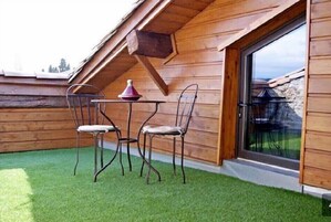 Una cabaña de madera con techo inclinado, una pequeña mesa con sillas y un ventanal grande.