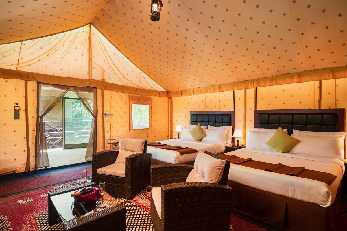 A tent-style room with two beds, wicker furniture, and a red carpet.