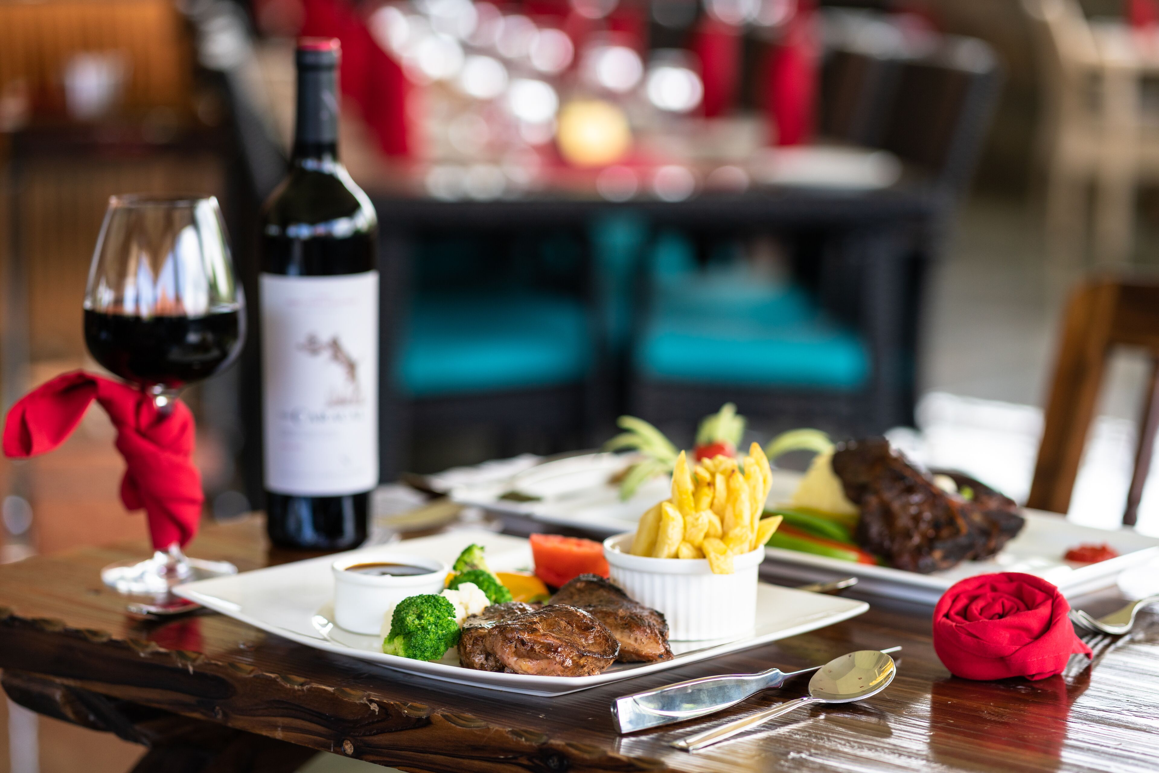 A dining table with a steak, fries, and a bottle of wine.