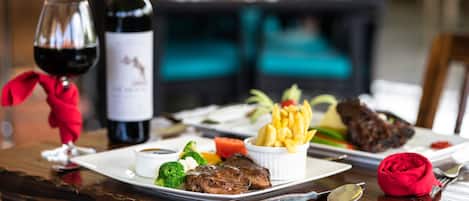 A dining table with a steak, fries, and a bottle of wine.