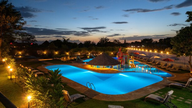 A swimming pool with a slide, lounge chairs, and a thatched-roof hut.