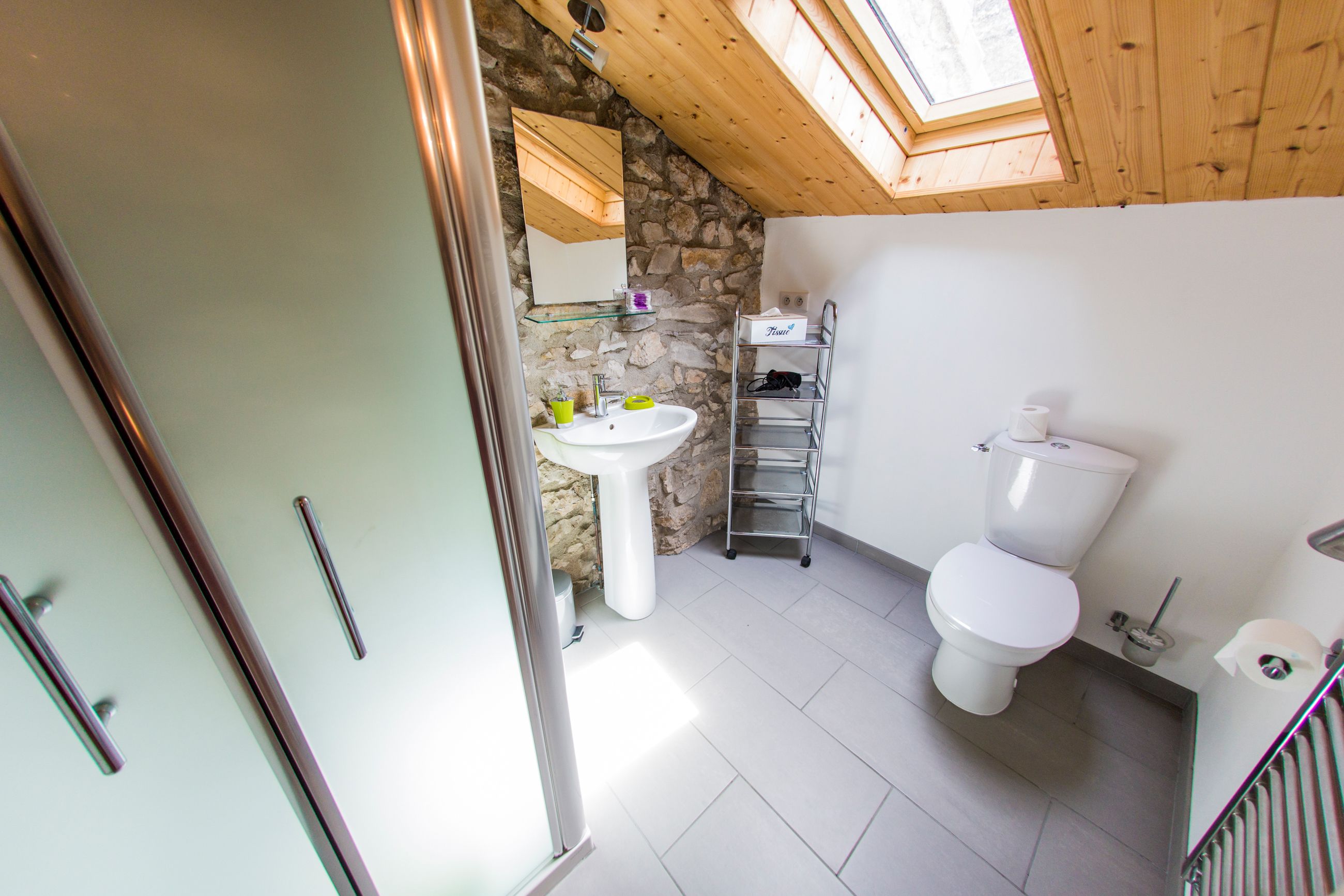 A bathroom with a stone wall, a skylight, a white sink, and a toilet.