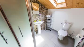 A bathroom with a stone wall, a skylight, a white sink, and a toilet.