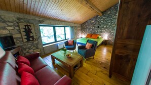 A cozy room with a stone wall, wooden ceiling, a red sofa, a wooden coffee table, and a bed with orange pillows. - Moulin d'Entre Les Roches (Puivert)