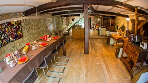 A dining area with a long table set for a meal, wooden beams on the ceiling, and a staircase leading to an upper level. - Moulin d'Entre Les Roches (Puivert)