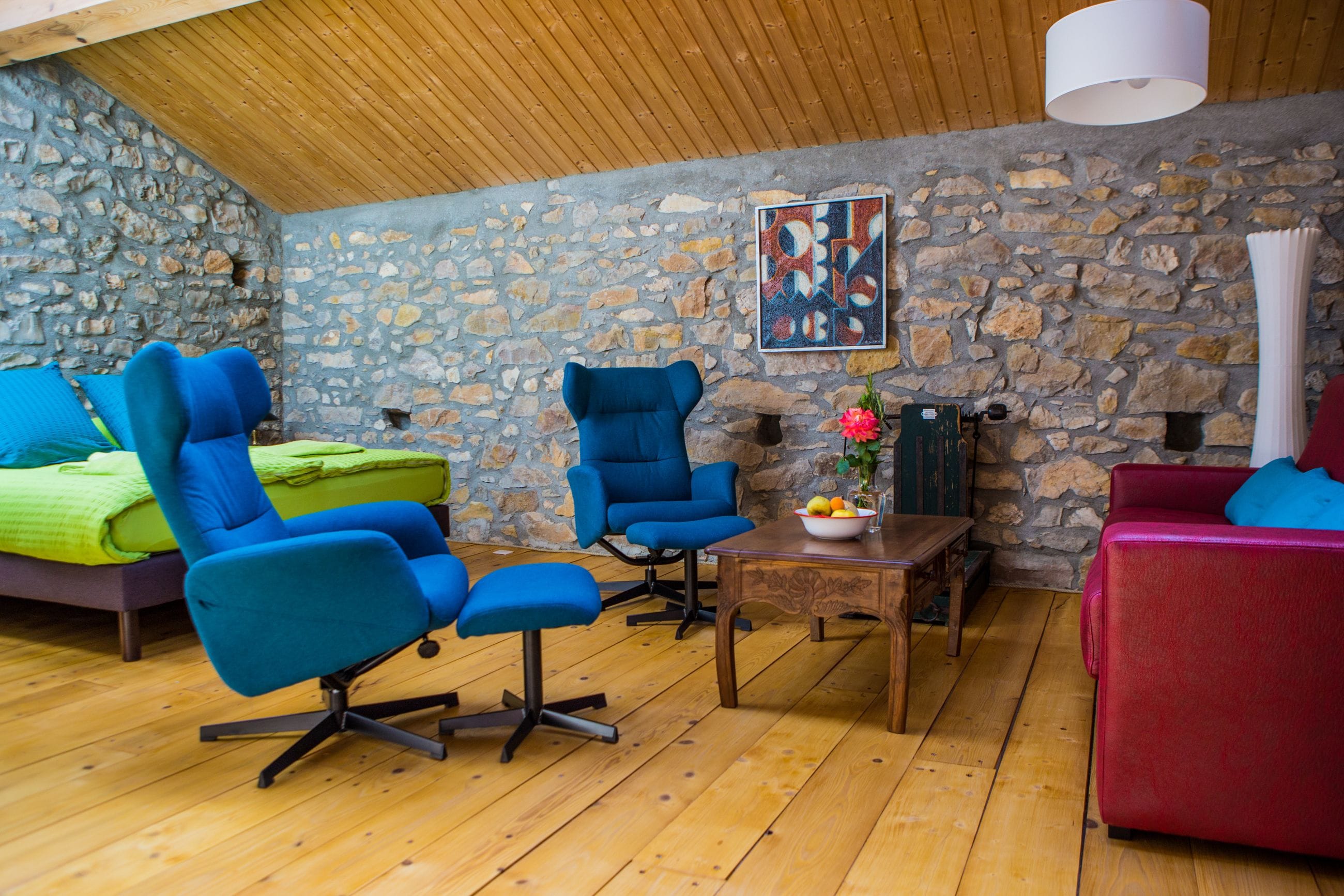A cozy room with a stone wall, wooden floor, and a mix of blue and red furniture.