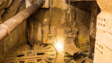 Primer plano de una habitación antigua de estilo industrial, con tuberías a la vista, un gran mecanismo de rueda y una viga de madera rústica.