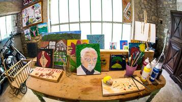 Une pièce où l’on trouve une table en bois sur laquelle sont exposées diverses peintures, un vélo et du matériel d’art.